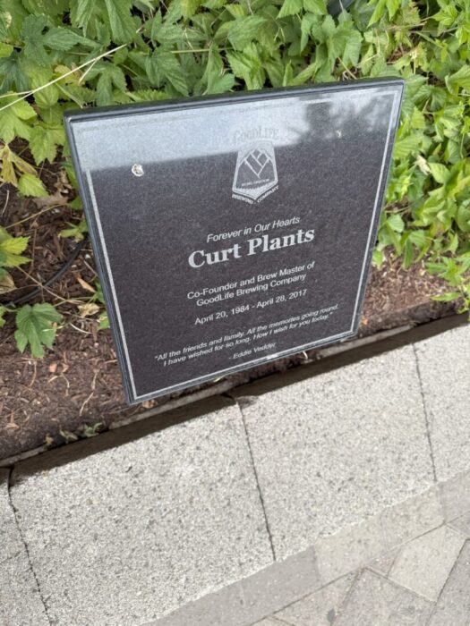 a Memorial Plaque Surrounded by Green Leafy Plants the Plaque Reads Forever in Our Hearts Curt Plants Co Founder and Brew Master of Goodlife Brewing Company April 20 1984 April 28 2017 the Plaque Includes a Quote and It Rests Beside a Concrete Sidewalk a Memorial Plaque Surrounded by Green Leafy Plants the Plaque Reads Forever in Our Hearts Curt Plants Co Founder and Brew Master of Goodlife Brewing Company April 20 1984 April 28 2017 the Plaque Includes a Quote and It Rests Beside a Concrete Sidewalk
