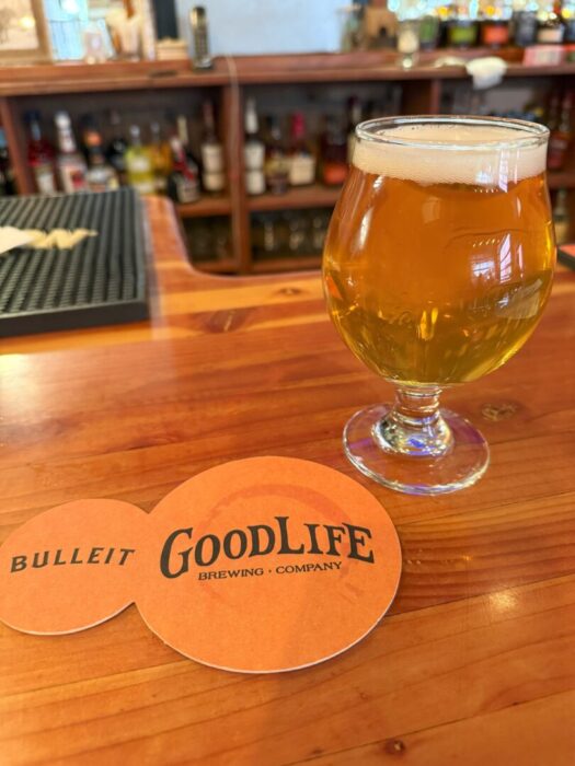a Round Glass of Golden Beer Sits on a Glossy Wooden Bar Next to an Orange Coaster That Reads Bulleit Goodlife Brewing Company Shelves with Liquor Bottles Are Blurred in the Background the Bar Has a Warm Inviting Atmosphere a Round Glass of Golden Beer Sits on a Glossy Wooden Bar Next to an Orange Coaster That Reads Bulleit Goodlife Brewing Company Shelves with Liquor Bottles Are Blurred in the Background the Bar Has a Warm Inviting Atmosphere