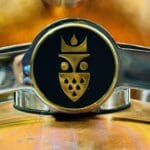 Close up of a Shiny Metallic Emblem with a Gold Geometric Face and Crown Design on Black Mounted on Copper and Steelits Symmetrical Shapes Echo the Sophistication Found in the Best Bars in Frederick Teardrop Patterns Add Elegance to the Piece