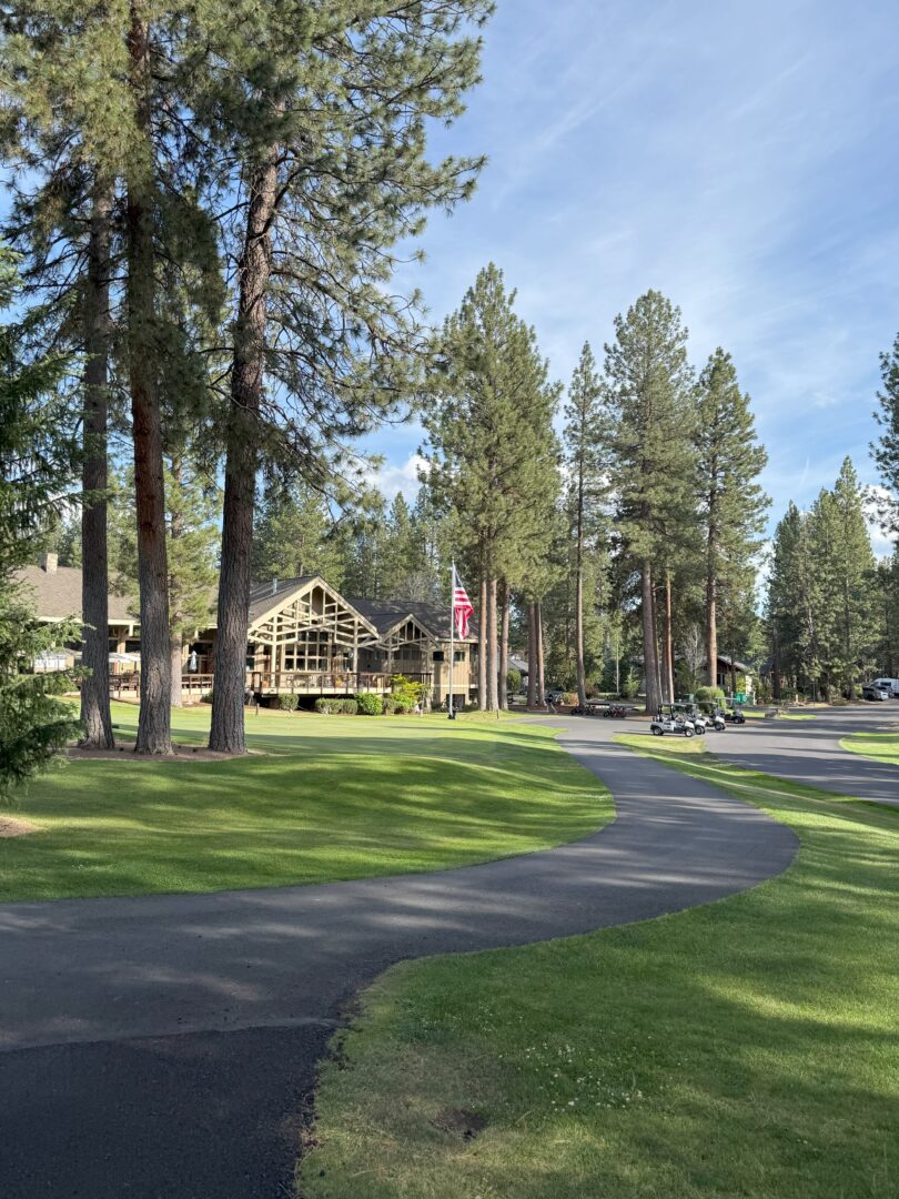 a Winding Paved Path Curves Through a Manicured Lawn with Tall Pine Trees in the Background Theres a Large Rustic Lodge with Many Windows an American Flag on a Pole and Golf Carts Parked Nearby Under a Clear Blue Sky a Winding Paved Path Curves Through a Manicured Lawn with Tall Pine Trees in the Background Theres a Large Rustic Lodge with Many Windows an American Flag on a Pole and Golf Carts Parked Nearby Under a Clear Blue Sky