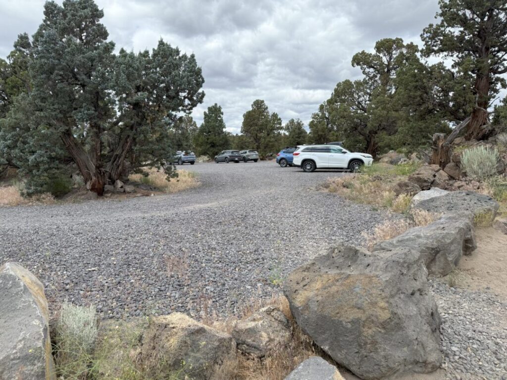 a Gravel Parking Lot with Several Cars Parked Among Scattered Juniper Trees Large Rocks Line the Front Edge and Sparse Grass and Brush Grow Around the Area the Sky is Cloudy Giving the Scene a Muted Overcast Look a Gravel Parking Lot with Several Cars Parked Among Scattered Juniper Trees Large Rocks Line the Front Edge and Sparse Grass and Brush Grow Around the Area the Sky is Cloudy Giving the Scene a Muted Overcast Look