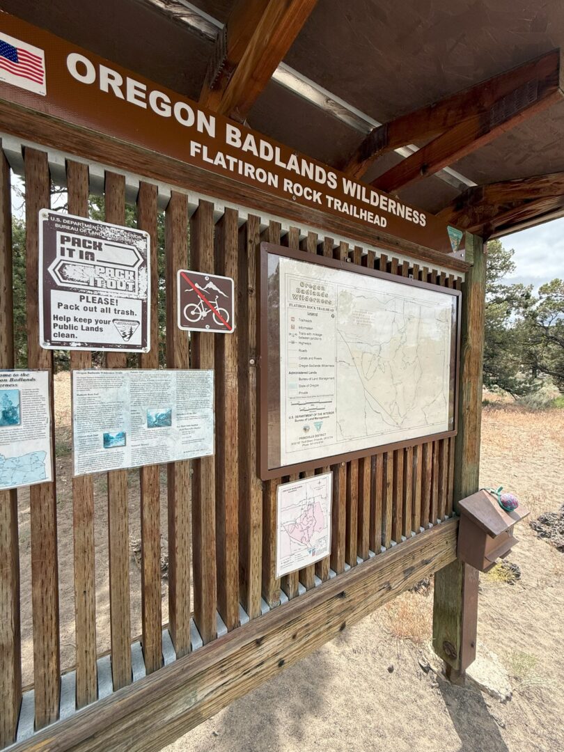 a Wooden Trailhead Sign for Oregon Badlands Wilderness at Flatiron Rock Shows Maps Information Signs and Notices Including a Pack It in Pack It out Reminder Sunlight Shines on the Display Dry Grass and Trees Are Visible in the Background a Wooden Trailhead Sign for Oregon Badlands Wilderness at Flatiron Rock Shows Maps Information Signs and Notices Including a Pack It in Pack It out Reminder Sunlight Shines on the Display Dry Grass and Trees Are Visible in the Background