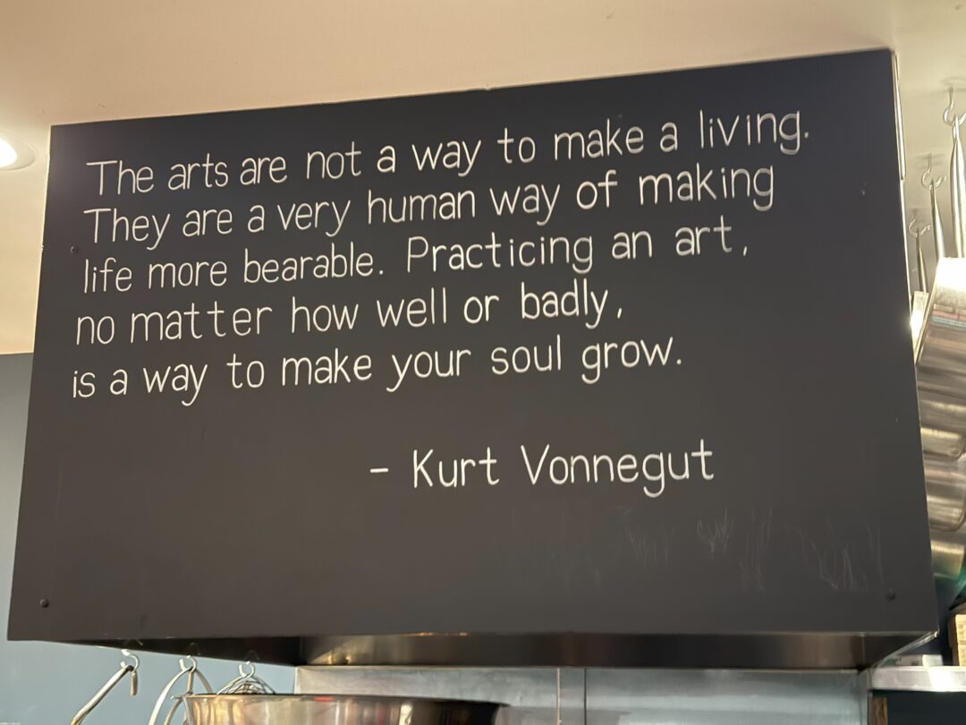 Kurt vonnegut market table bistro a Black Sign with White Typewritten Text Reads the Arts Are Not a Way to Make a Living at Market Table Bistro Theyre Seen As a Very Human Way of Making Life More Bearablea Practice That Helps Your Soul Grow Kurt Vonnegut