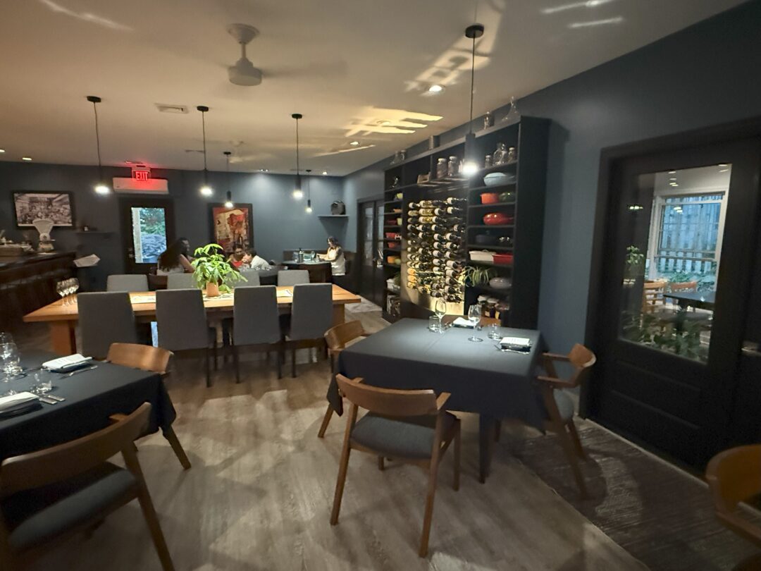 Market table bistro interior a Modern Restaurant Interior with Dark Walls Wooden Floors and Neatly Set Tables Market Table Bistro Features Wine Racks Shelves with Dishes Contemporary Chairs Soft Lighting and Large Windows Some Tables Are Pushed Together for Group Seating