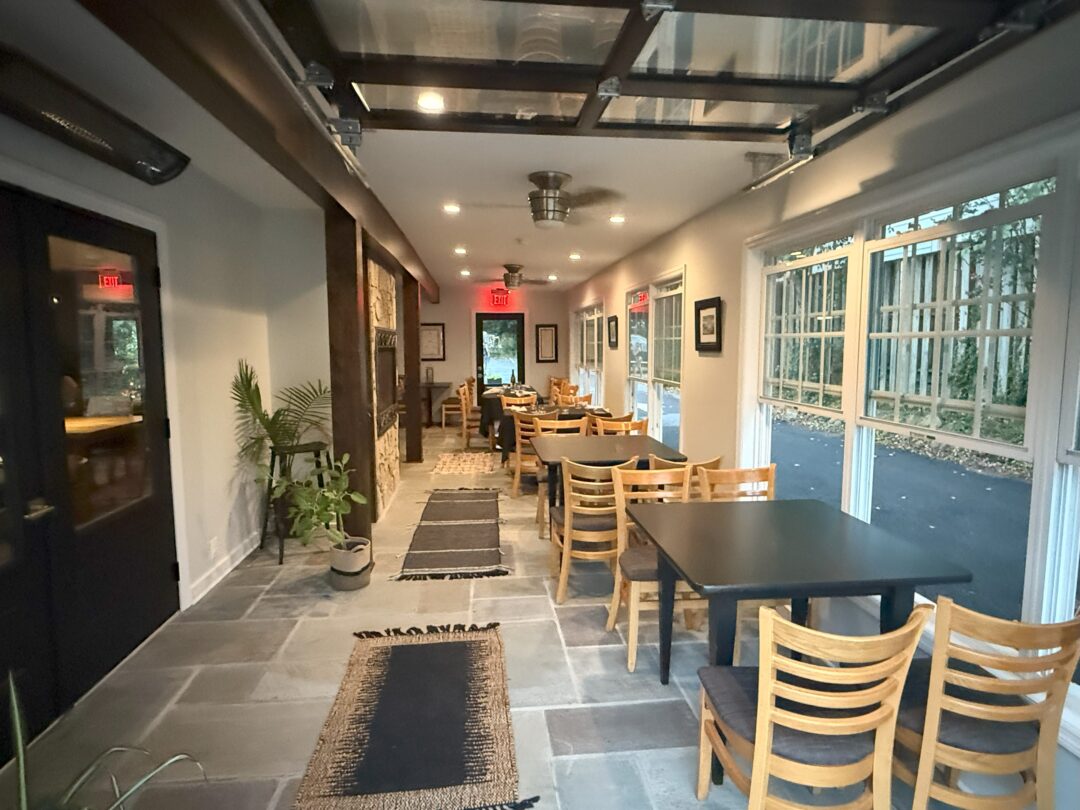 Market table bistro patio a Cozy Modern Dining Area at Market Table Bistro Features Wooden Chairs and Black Tables in a Narrow Room Large Windows Fill the Space with Natural Light Highlighting Potted Plants Wall Art Rugs on the Stone Floor and Glass Doors at Both Ends