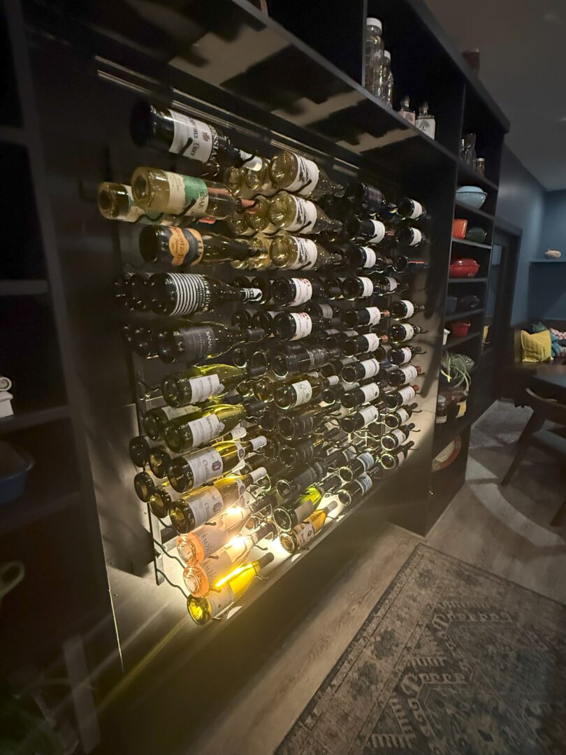 Market table bistro wine rack a Wall mounted Wine Rack at Market Table Bistro Holds Dozens of Wine Bottles Arranged Horizontally on Sleek Black Metal Shelves Dim Lighting Shelves with Glassware and Bowls and a Patterned Rug Complete the Inviting Wooden floored Room