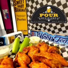 Pour Decisions New Market Md a Black Basket Lined with Checkered Paper Holds Saucy Buffalo Chicken Wings Celery Sticks and Two Cups of Ranch Behind the Basket Are Craft Beer Cans and a Visible Pour Decisions Signserving Up Flavor in New Market Md