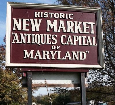 Antiques New Market Maryland a Large Maroon and White Roadside Sign Reads Historic New Market Antiques Capital of Maryland the Sign Stands on Wooden Posts Among Trees and Blue Sky Marking the Charm of New Market Md As a Notable Destination
