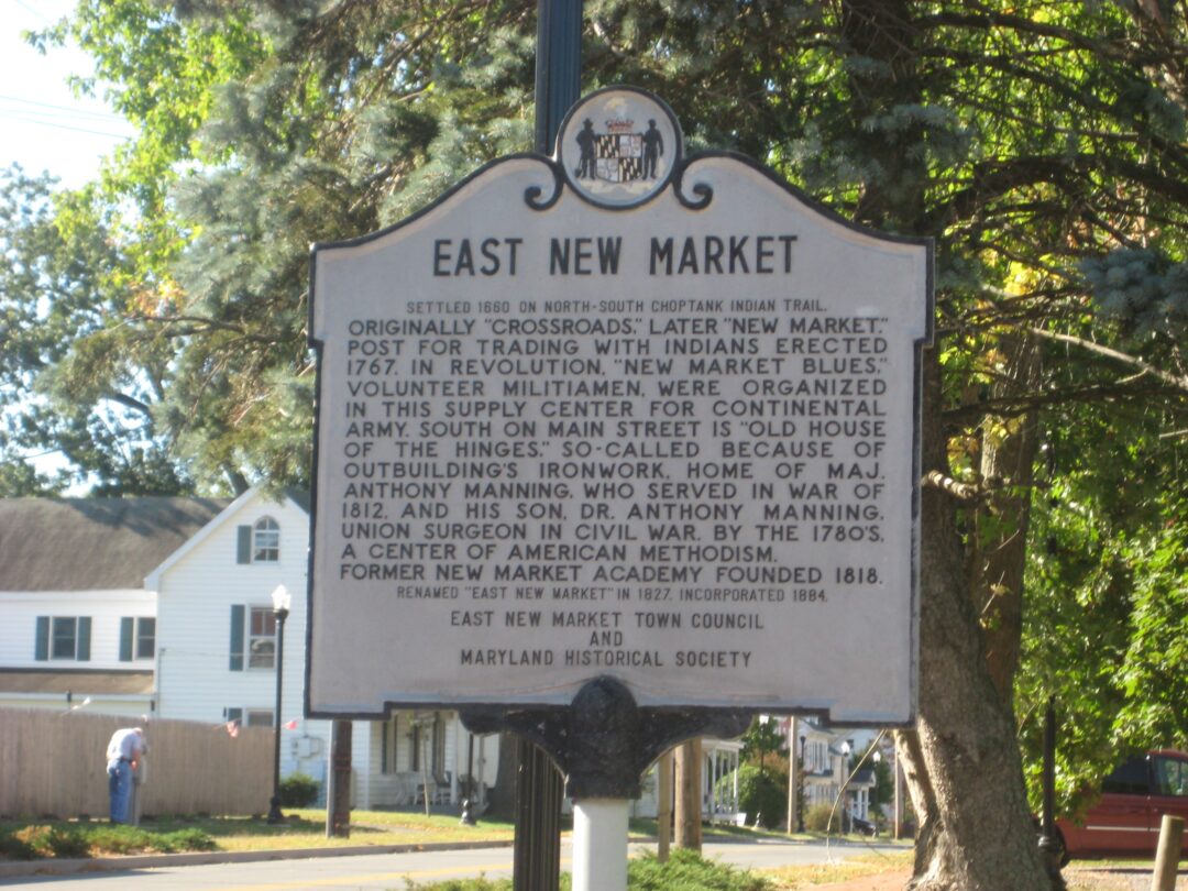 East New Market Marker a Historical Marker for East New Market Md Stands by a Street the Sign Details the Towns Origins Role in the American Revolution and War of 1812 and Mentions Dr Anthony Manning Trees and a House Are Visible in the Background on a Sunny Day