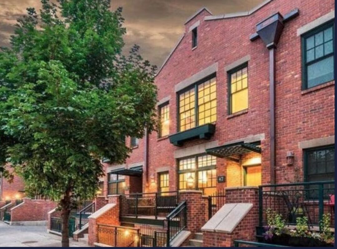 Modern studio old mill district bend a Row of Modern Brick Townhouses at Dusk with Large Lit Windows and Black Railings Lining Small Front Stepsthese Inviting Homes Evoke the Charm Youd Seek when Deciding Where to Stay in Bend Oregon a Leafy Tree Completes the Picturesque Scene