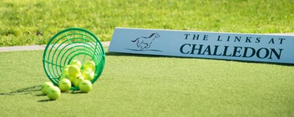 Links at Challedon Practice Area a Green Basket Tipped over on Artificial Turf Spills Tennis Balls in the Background a White Sign with a Horse Graphic Reads the Links at Challedon Highlighting This Vibrant Outdoor Sports Area Surrounded by Blurred Green Grass