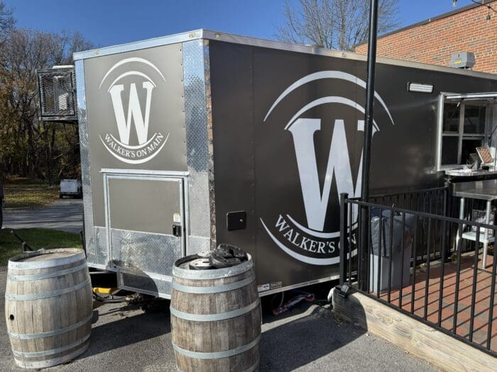 a Black Food Truck with Large White W Logos and Walkers on Main Text is Parked Beside a Brick Building in Mt Airy Md Two Wooden Barrels Stand in Front with a Black Railing on the Right and Trees with Bare Branches in the Background