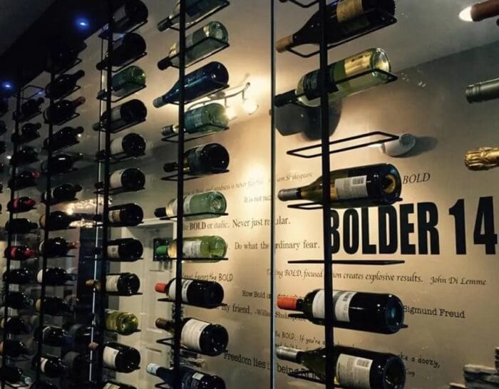 a Modern Wine Cellar in Mt Airy Md Features Bottles Stored Horizontally on Black Metal Racks Mounted to a Glass Wall Inspirational Quotes in Various Fonts Decorate the Wall While Warm Lighting Highlights the Bottles and Text