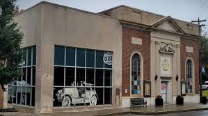 Liquidity Aleworks Mt Airy a Two Story Brick and Concrete Building in Mt Airy Md with Large Windows on the Left Side Displaying a Mural of a Vintage Car the Right Side Features Classical Architectural Details a Triangle Pediment a Clock and Arched Windows a Bench Sits Outside the Entrance