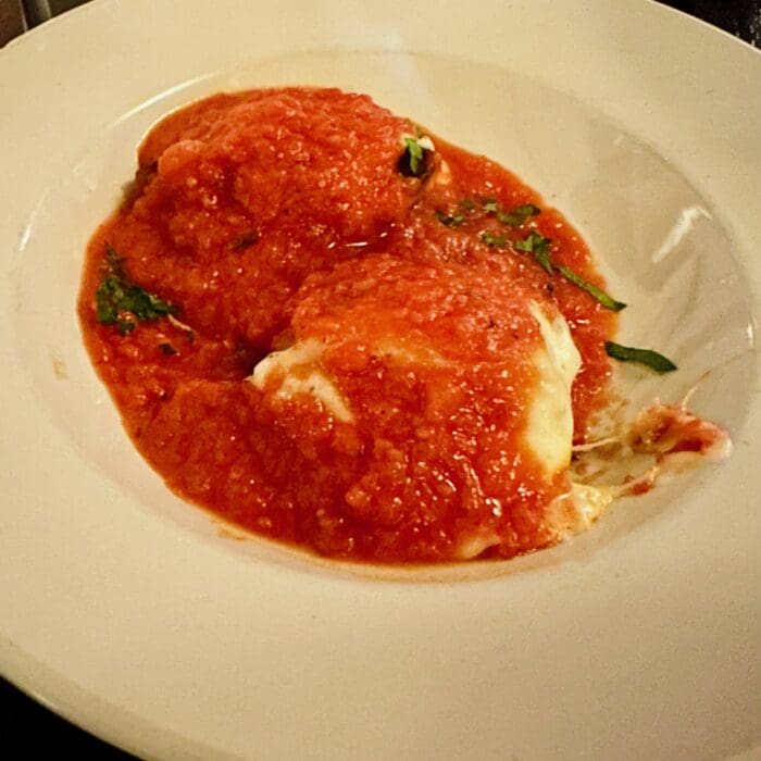 Two Large Ravioli Topped with Chunky Red Tomato Sauce and Chopped Green Herbs Are Served on a White Plate at Cucina Massi Frederick Md Melted Cheese Peeks Through with Clean Edges and Slight Sauce Drips Along One Side