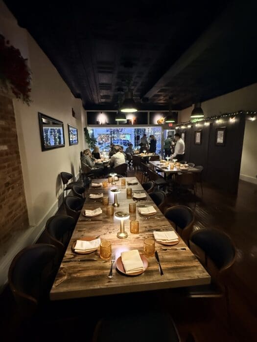 Long Wooden Dining Table in a Cozy Dimly Lit Restaurant with Candles and Napkins Set for Guests Rows of Chairs on Both Sides