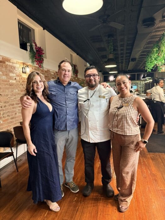 Four Smiling Adults Posing Together in a Restaurant with Exposed Brick Wall and Hanging Plants