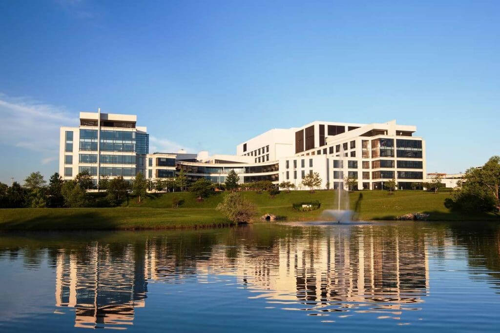 Modern White Office Buildings Along a Grassy Bank by a Calm Lake with a Fountain and Reflections in the Water
