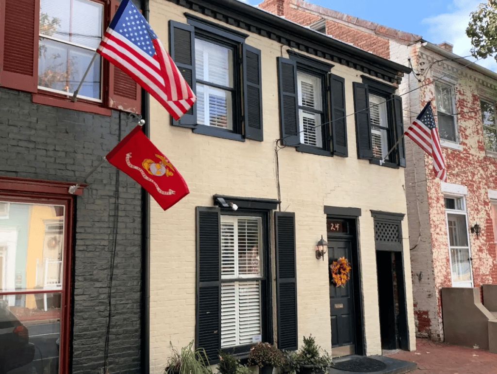 Two Story Brick House with Dark Shutters White Front Door and Two American Flags Plus a Red Marine Corps Flag Outside the Window Wreath on the Door
