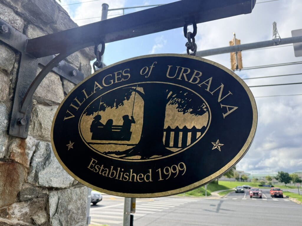 Round Black Circular Sign with a Gold Border Hanging from a Stone Wall Features a World Map and the Text Established 1999
