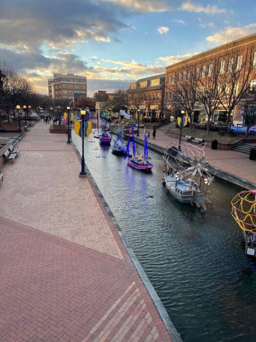 Canal in a city with colorful moored boats along a brick pedestrian walkway at sunset/sunlit late afternoon.