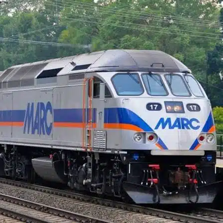Diesel Electric Marc Locomotive Number 17 on Railroad Tracks with Green Trees in the Background Silver Body with Blue and Orange Stripes