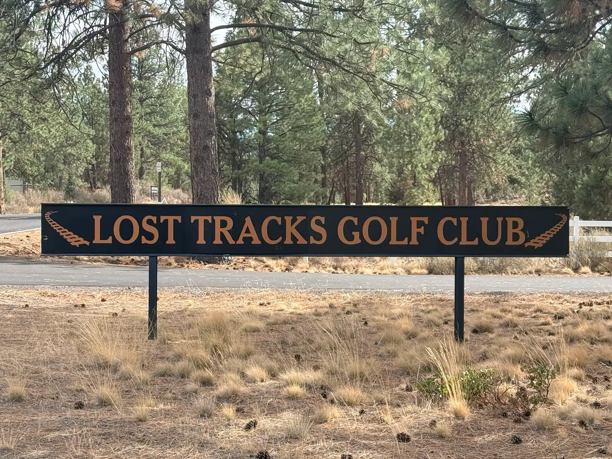 Sign Reads Lost Tracks Golf Club with a Railroad Track Graphic Set Against a Background of Pine Trees and Dry Grass