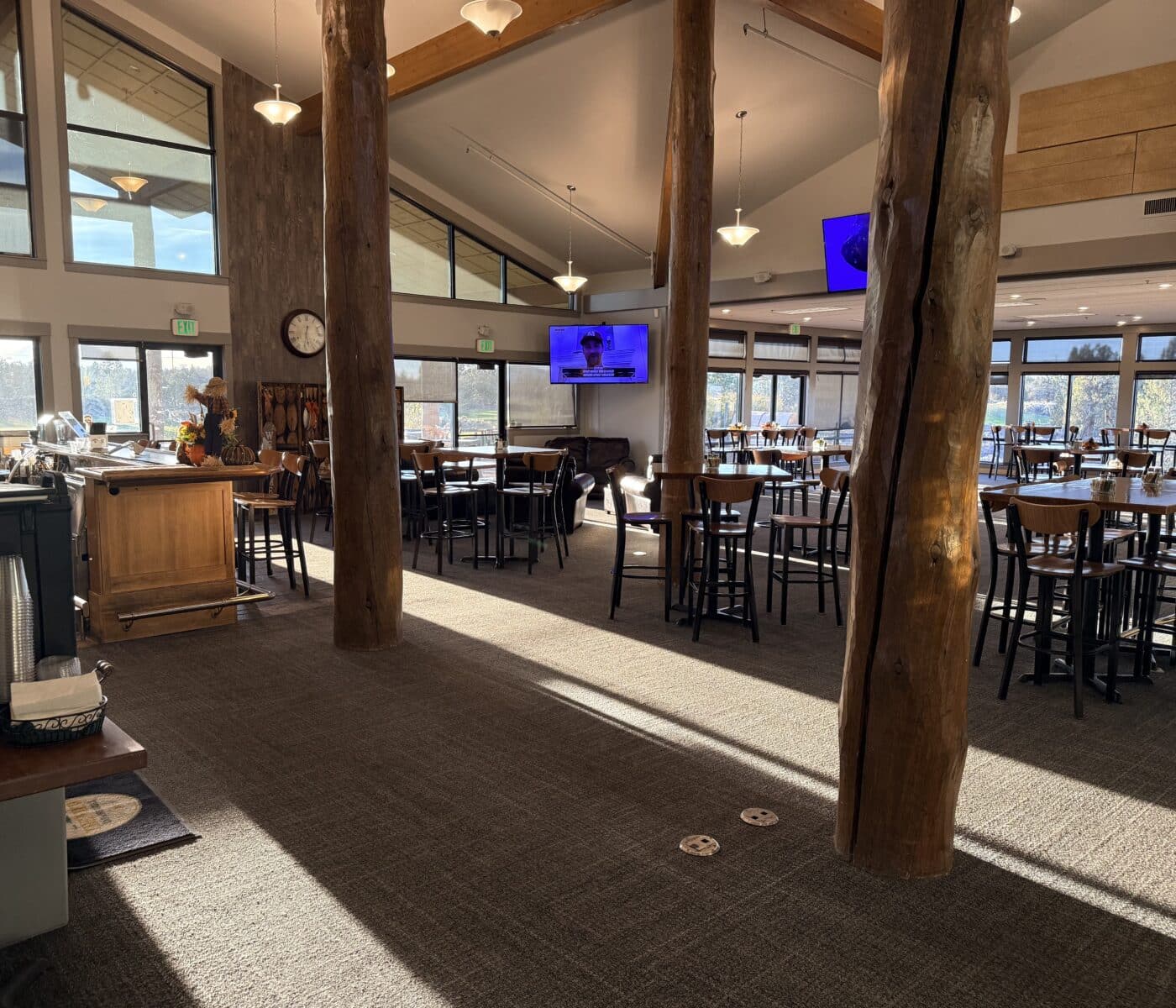 Open Dining Area with Tall Wooden Columns Multiple Tables and Chairs Large Windows and Hanging Lights in a Rustic Restaurant