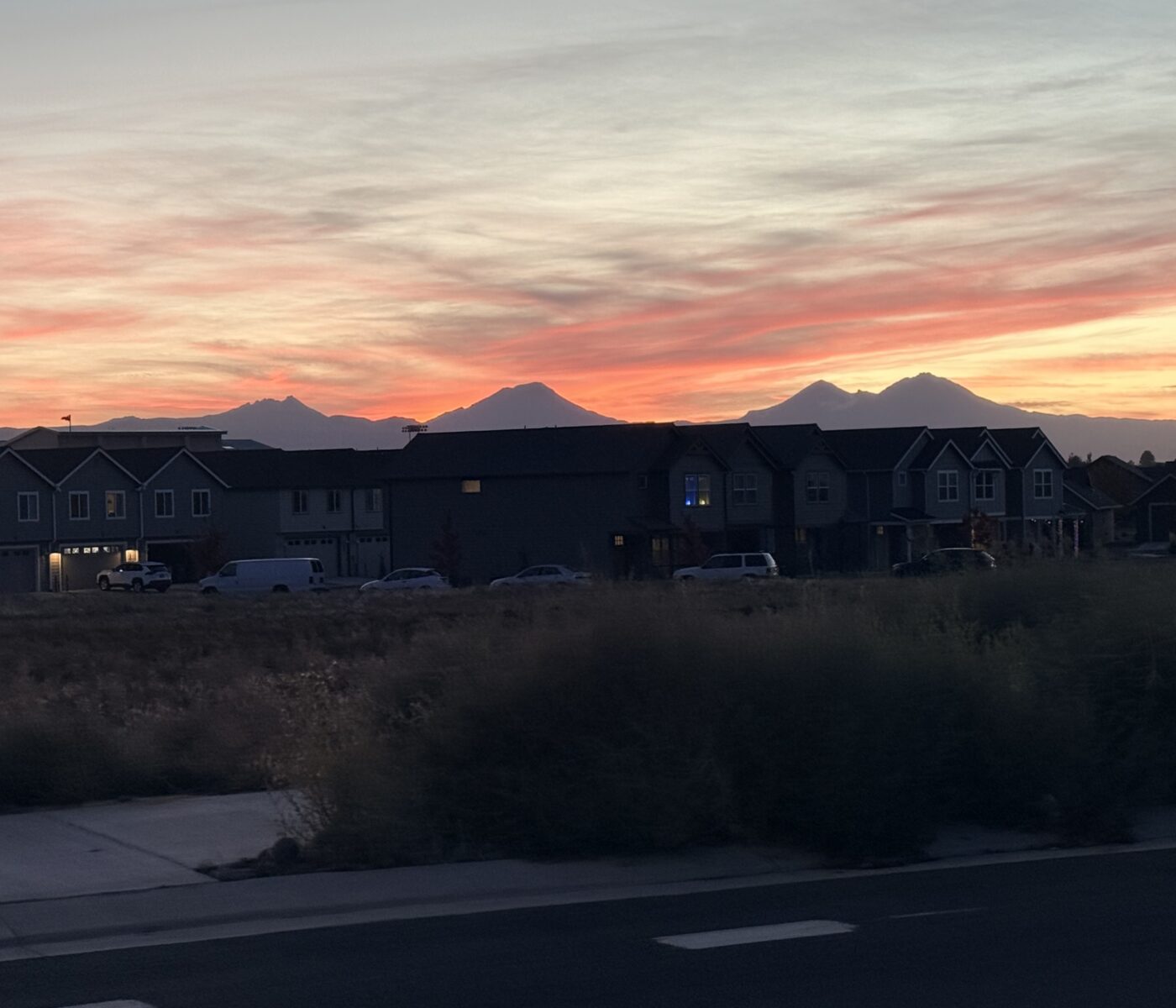 Suburban Street at Dusk with Row of Townhouses and a Distant Mountain Range Silhouetted Against a Pink Orange Sunset Sky
