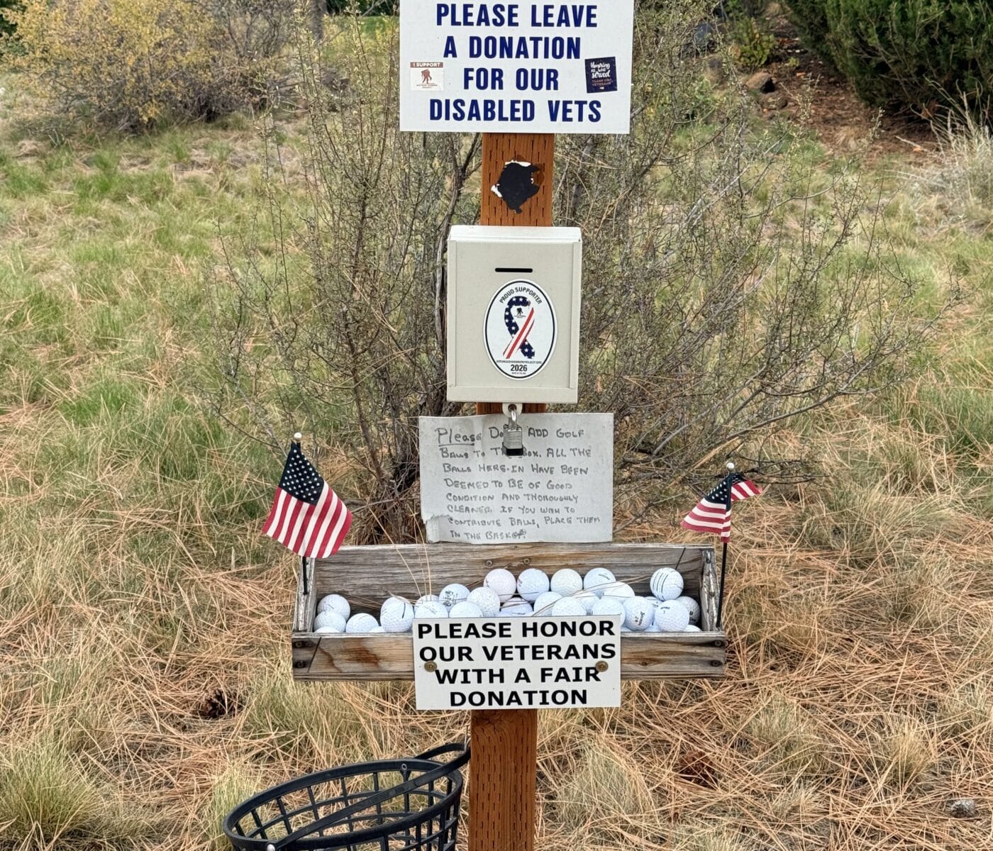 Wooden Post with a Large Sign Asking to Take a Ball or Two and Donate for Disabled Veterans Basket of Golf Balls and Small American Flags Nearby
