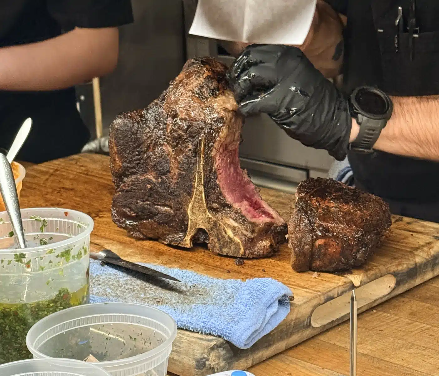 Chef Wearing Black Gloves Carves a Large Smoked Beef Roast on a Wooden Cutting Board