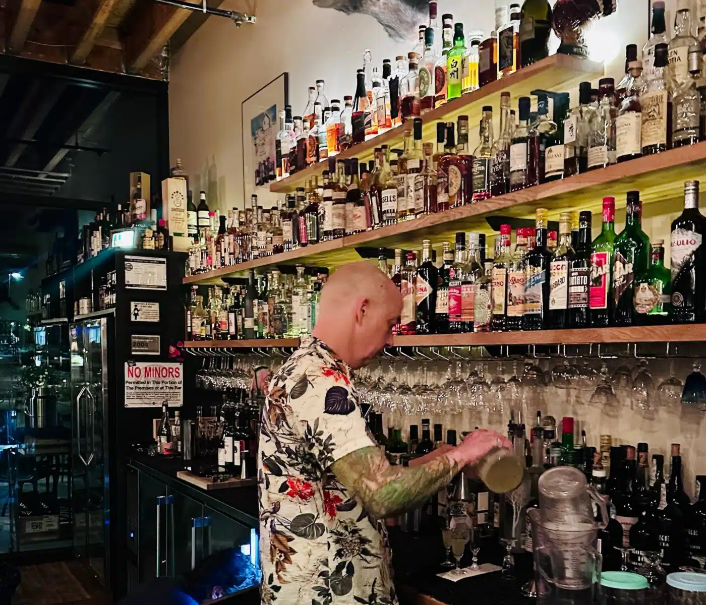 Bartender Wearing a Tropical Shirt Behind a Long Shelf of Liquor Bottles in a Bar