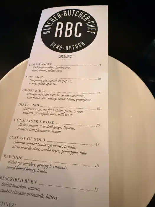 Cocktail Menu with a Round Rbc Logo at the Top and Drink Names Like Law Ranger and Ghost Rider Listed Below on a Plate Surface