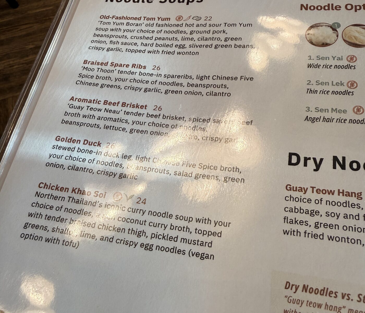 a Close up View of a Sen Thai Noodles Menu Page Titled Noodle Soups Listing Options Including Tom Yum Braised Spare Ribs Aromatic Beef Brisket Golden Duck and Chicken Khao Soi with Their Ingredients Plus a Column Showing Three Noodle Varieties