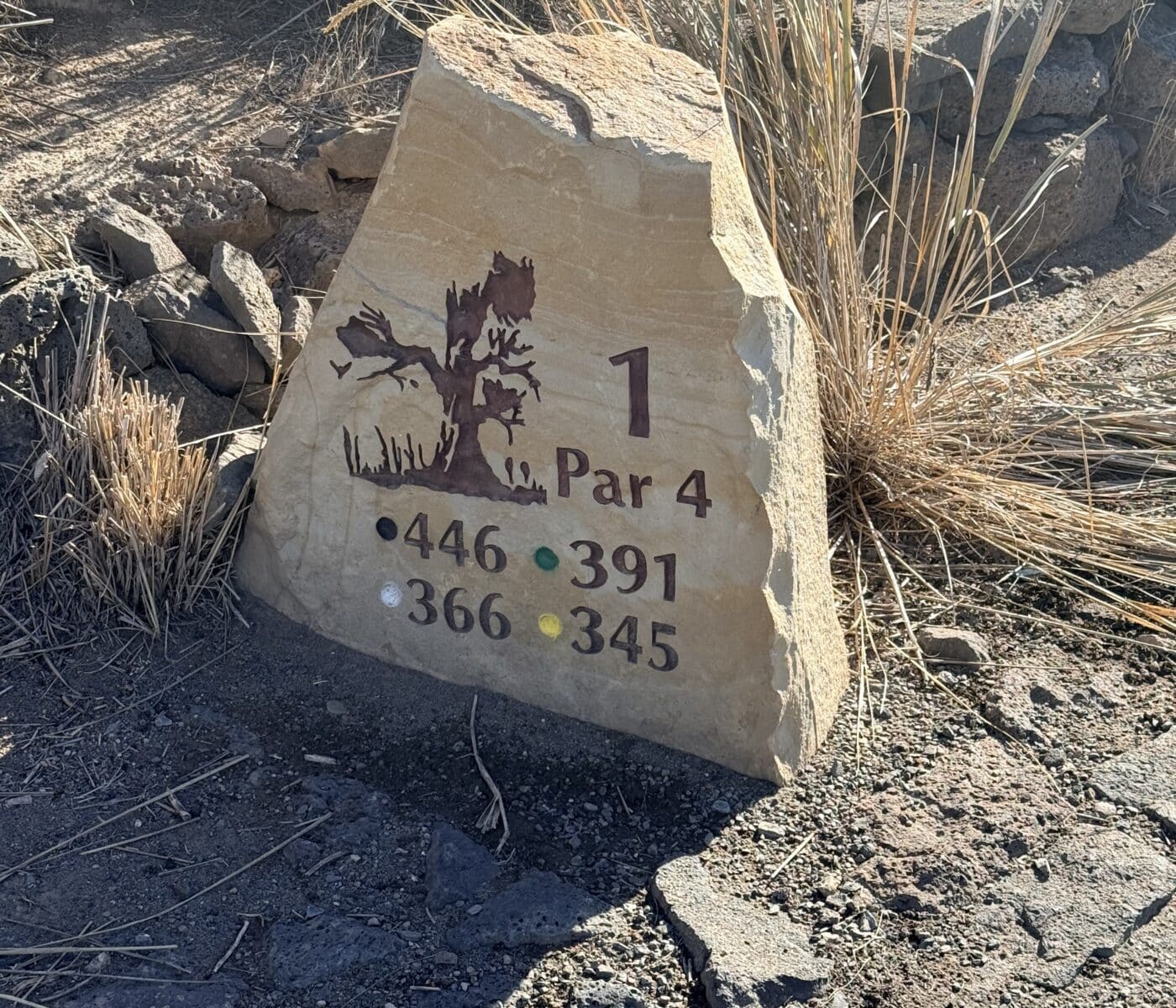 a Jagged Tan Tee Marker Stone at Juniper Golf Course Displays the Number 1 Par 4 and Distances for Four Colored Tees Set into Dry Ground Surrounded by Tall Withered Grass