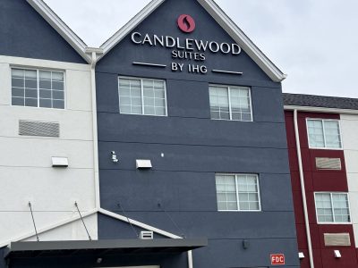 Exterior of Candlewood Suites by IHG hotel with a dark blue facade, white trim, and glass lobby doors at the entrance.