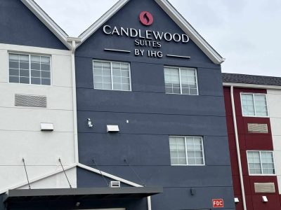 Exterior of Candlewood Suites by IHG hotel with a dark blue facade, white trim, and glass lobby doors at the entrance.