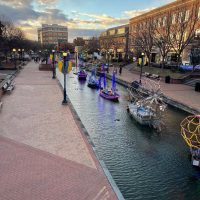 Canal in a city with colorful moored boats along a brick pedestrian walkway at sunset/sunlit late afternoon.