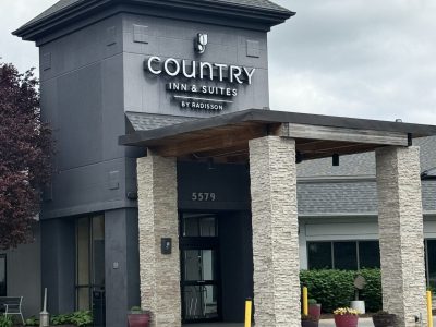 Front entrance of a Country Inn & Suites by Radisson, with tall stone columns and planters nearby.