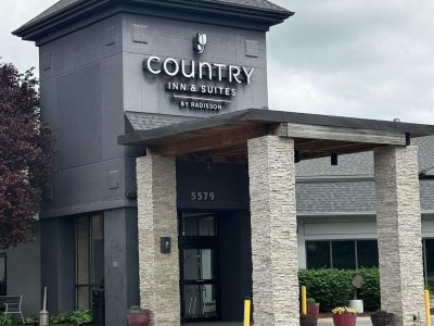 Front entrance of a Country Inn & Suites by Radisson, with tall stone columns and planters nearby.