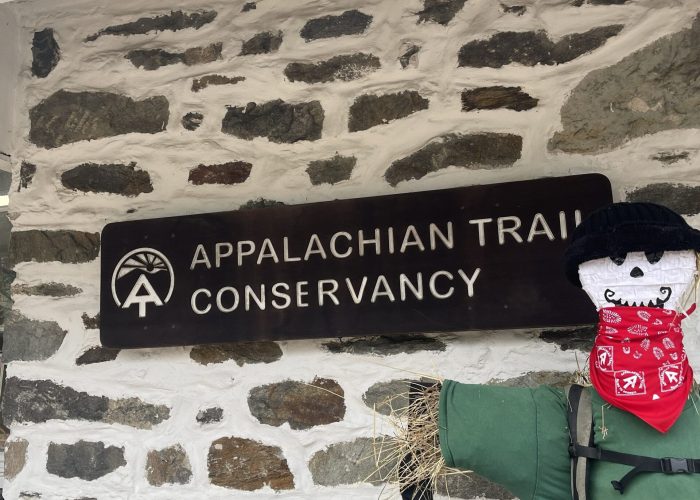 Stone wall with a sign reading Appalachian Trail Conservancy and a green hiking backpack strapped to the right.
