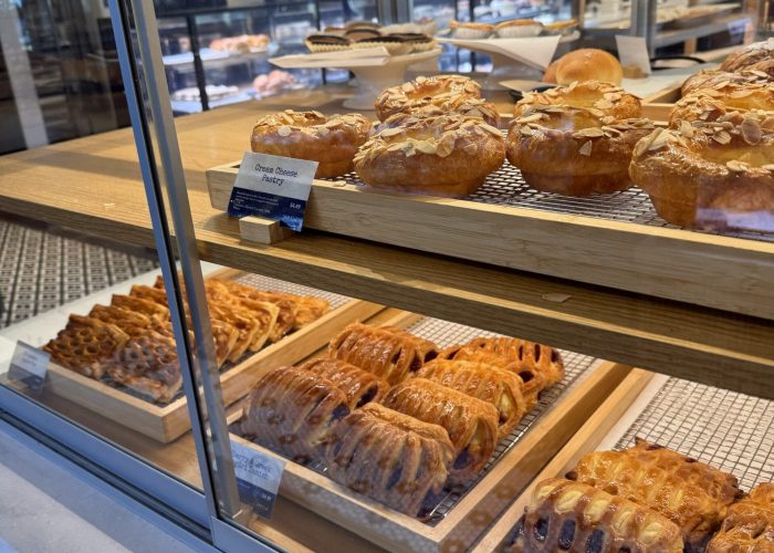 A bakery display case with shelves holding various pastries—a tempting sight often found in coffee shops in Frederick MD. The top shelf features round pastries topped with sliced almonds, and the lower shelves are lined with flaky, golden-brown treats.