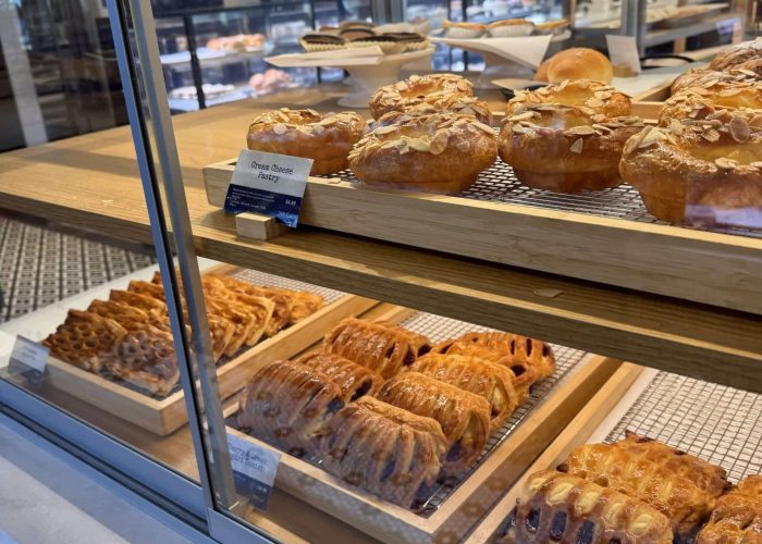 A bakery display case with shelves holding various pastries—a tempting sight often found in coffee shops in Frederick MD. The top shelf features round pastries topped with sliced almonds, and the lower shelves are lined with flaky, golden-brown treats.