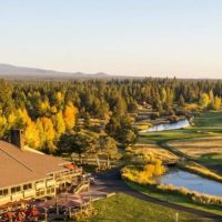 Sunriver-resort-place-to-stay-bend-oregon The Sunriver Lodge at Sunriver Resort with its golf course is surrounded by lush green fairways and autumn-colored trees—a picturesque choice for those seeking where to stay in Bend, Oregon, with mountain views under a golden sunset sky.