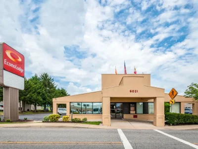 Econo Lodge hotel exterior with red sign, beige entrance, flags on the roof, and a pedestrian crossing sign against a cloudy blue sky.